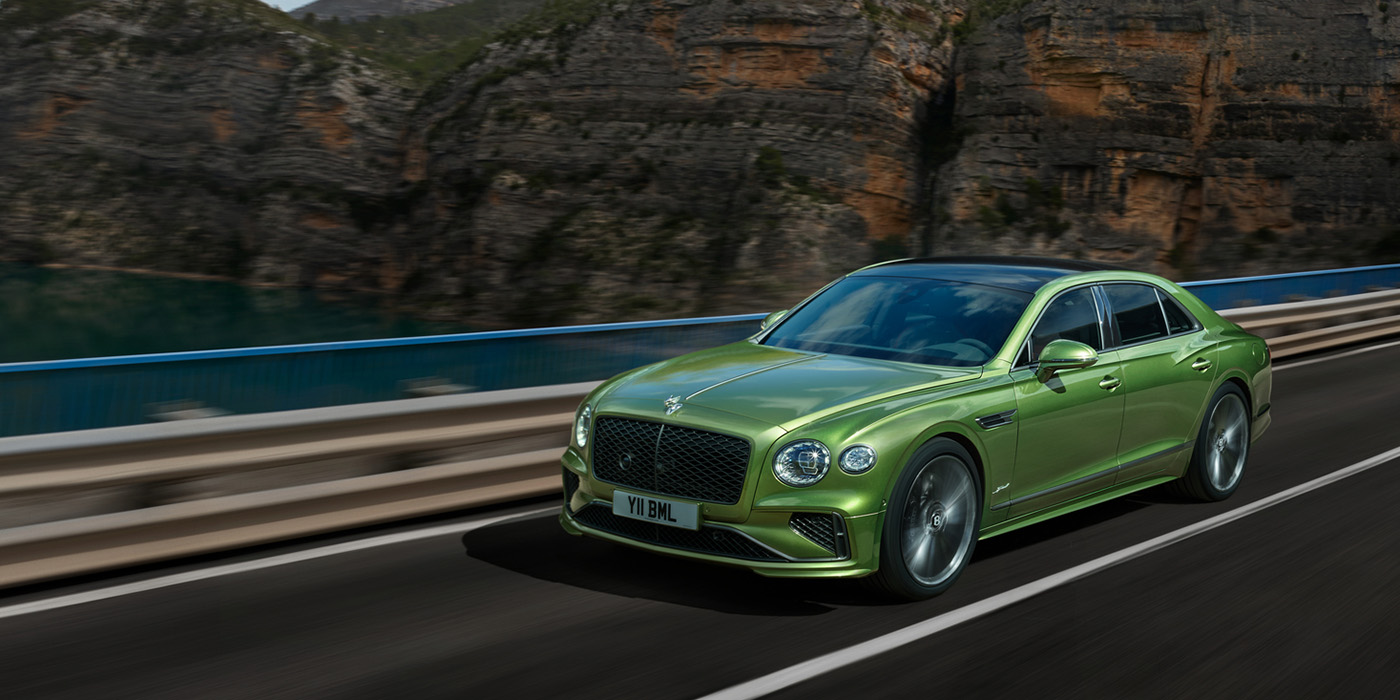 Bentley Basel Bentley New Flying Spur Speed v8 hybrid sedan driving dynamically on a mountain road in Tourmaline Green paint