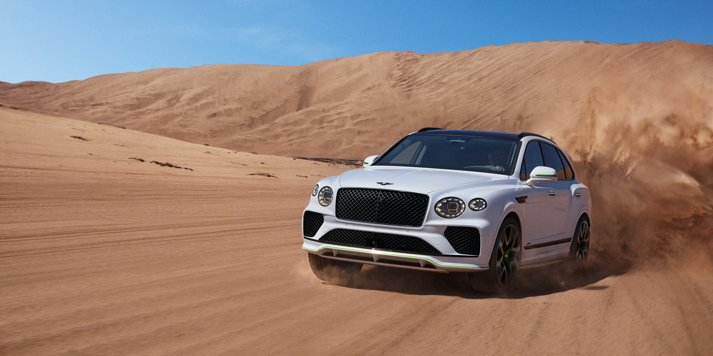 Bentley Basel Bentley Bentayga Speed SUV front three quarter in Snow Quarts Pearlescent by Mulliner white paint driving dynamically through the desert