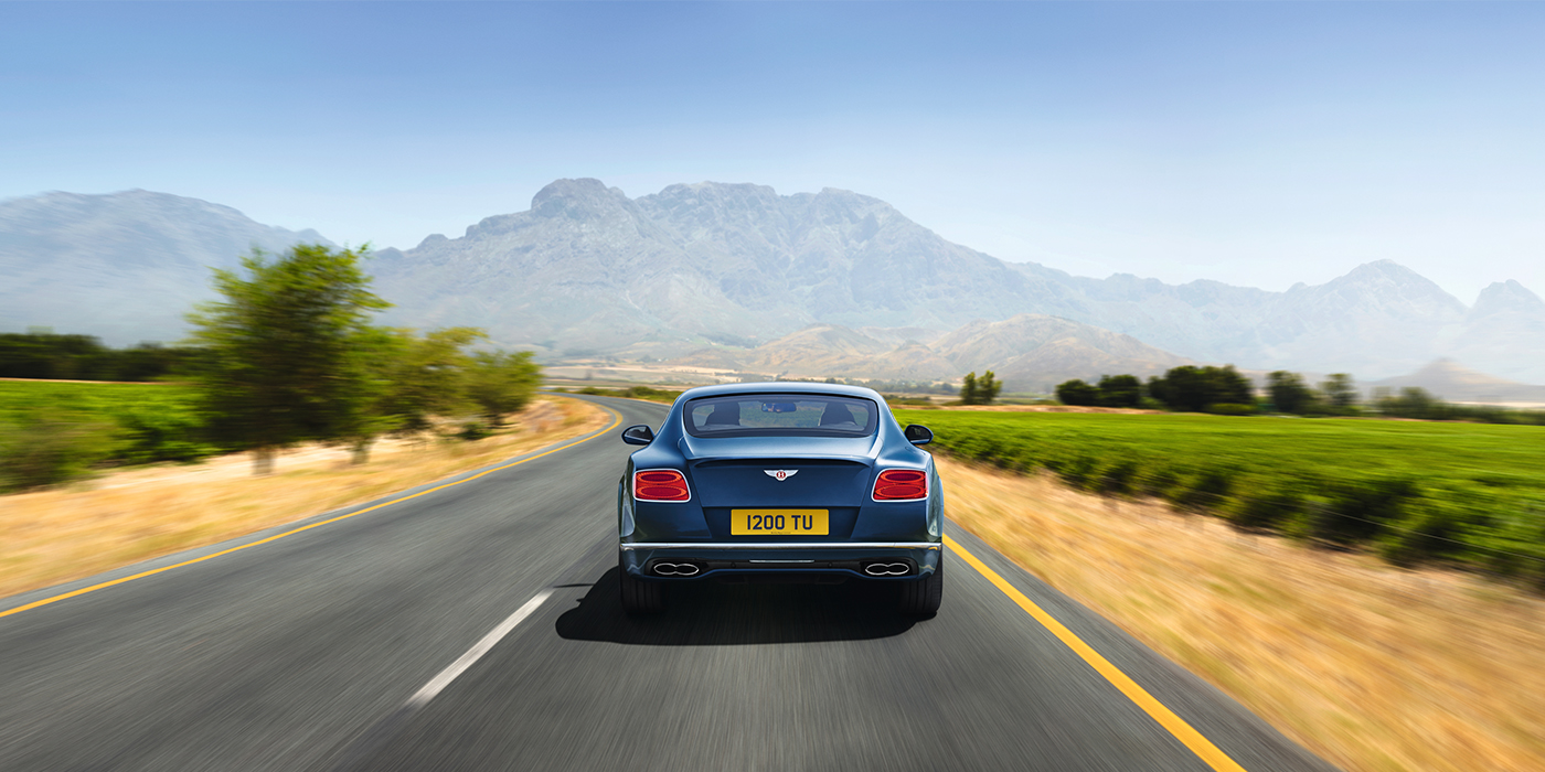 Bentley Basel Bentley Pre Owned Bentley Continental GT in Marlin blue paint seen from rear on country road