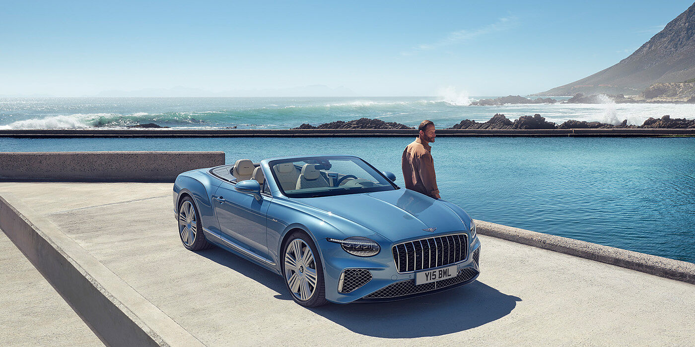 Bentley Basel New Bentley Continental GTC Azure convertible front view in Light Windsor blue paint with 22 inch ten spoke wheels parked by the sea in the sunshine