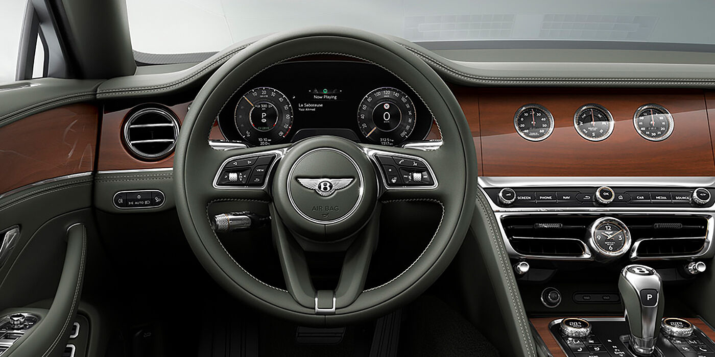 Bentley Basel New Bentley Flying Spur sedan front cabin in Cumbrian Green hide and Crown Cut walnut veneer showing steering wheel and Rotating Display with three clocks on face