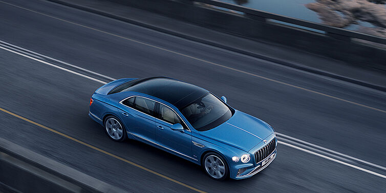 Bentley Basel New Bentley Flying Spur Azure sedan in Light windsor blue paint by Mulliner, with 22 inch Azure wheels seen from overhead driving dynamically on a country road