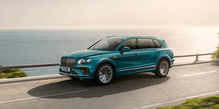 Bentley Basel Bentley Bentayga Extended Wheelbase Azure SUV in Topaz blue paint driving dynamically by the ocean