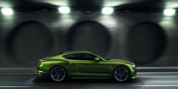 Bentley Basel Bentley Continental GT Speed coupe profile in Tourmaline Green drivig dynamically past a concrete wall at night