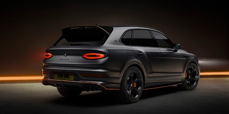 Bentley Basel Bentley Bentayga S Black Edition SUV rear three quarter in Anthracite Satin paint against a dark red and yellow background