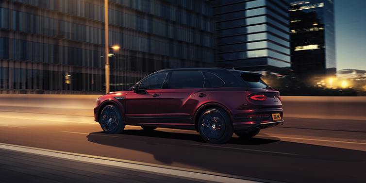Bentley Basel Bentley Bentayga Extended Wheelbase Mulliner SUV in Cricket Ball red paint driving dynamically in city at night