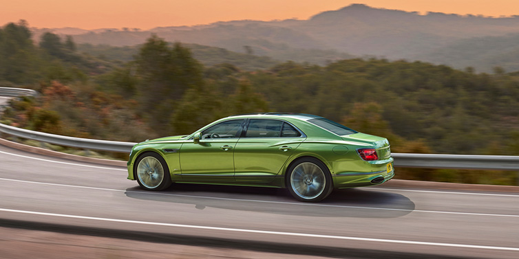 Bentley Basel Bentley Flying Spur Speed sedan side profile in Tourmaline Green paint driving dynamically on a mountain road at sunset