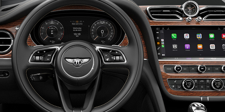 Bentley Basel Bentley Bentayga SUV front interior detail of steering wheel and driver screens surrounded by Beluga black hide and Crown Cut Walnut veneer