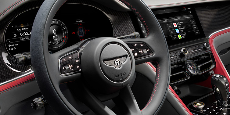 Bentley Basel Bentley Flying Spur Speed sedan front interior detail showing steering wheel and driver screens surrounded with Hotspur red and Gravity Grey hides